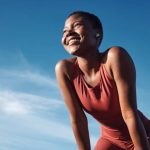 Fitness, black woman and happy athlete smile after running, exercise and marathon training workout. Blue sky, summer sports and run of a African runner breathing with happiness from sport outdoor